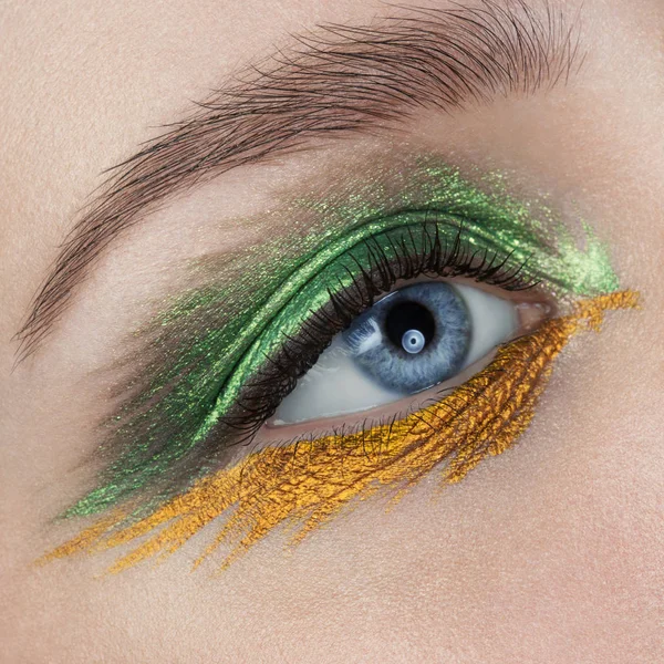 close up blue eye with golden and green eye shadow