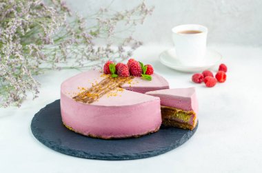 Ahududulu kek, beyaz arka planda, tahta tabakta kesilmiş bir parça. Yakın plan. Karamel serpiştirilmiş fıstıklı.