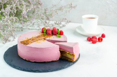 Ahududulu kek, beyaz arka planda, tahta tabakta kesilmiş bir parça. Yakın plan. Karamel serpiştirilmiş fıstıklı.