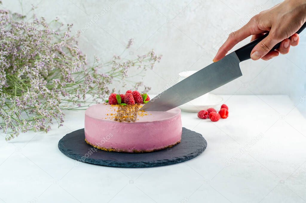 Raspberry cake. Vegan, vegetarian dessert is cut by the hand of the cook with a knife. Healthy sweets.