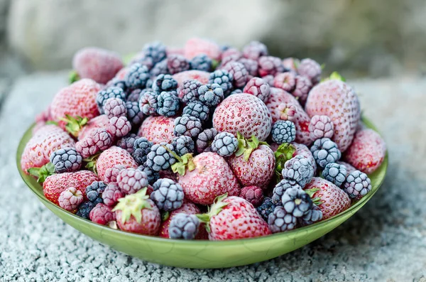 Eine Mischung aus gefrorenen Erdbeeren, Brombeeren, Himbeeren, die mit Raureif auf einem Teller bedeckt sind. Nahaufnahme, Seitenansicht — Stockfoto