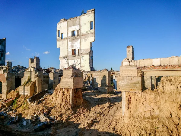 The ruins of a large destroyed building, pieces of stone, concrete, clay and metal against the blue clear sky. — Stock Photo, Image