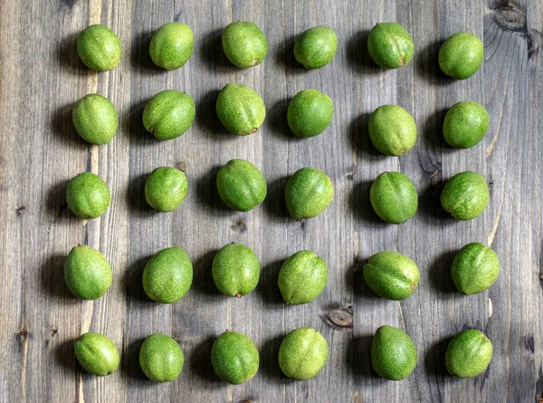 Młode zielone owoce orzechów włoskich leżą w rzędach na szarym drewnianym tle. — Zdjęcie stockowe