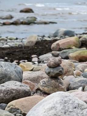 Küçük bir kule gibi üst üste yığılmış taşlar ve kayaların olduğu gerçekçi bir deniz fotoğrafı. Kayaların ve sahil çevresinin doğal dokuları yumuşak, doğal ışıklandırmayla vurgulanarak, barışçıl ve dengeli bir sahne yaratılıyor..