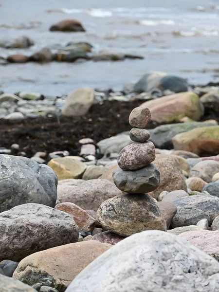 Küçük bir kule gibi üst üste yığılmış taşlar ve kayaların olduğu gerçekçi bir deniz fotoğrafı. Kayaların ve sahil çevresinin doğal dokuları yumuşak, doğal ışıklandırmayla vurgulanarak, barışçıl ve dengeli bir sahne yaratılıyor..