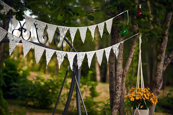 Aralarında beyaz bayrak çelenkleri olan ağaçların gerçekçi bir fotoğrafı. Yumuşak doğal ışık, bayrakları ve çevreleyen yeşillikleri vurguluyor. Kutlama ve sakin bir açık hava ortamı yaratıyor..