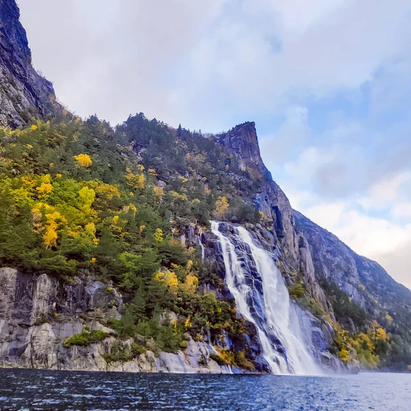 Realistic photograph of Norwegian fjords in autumn, showcasing dramatic mountains, calm water reflections, and vibrant fall colors. Authentic nature scenery captured in Norway.