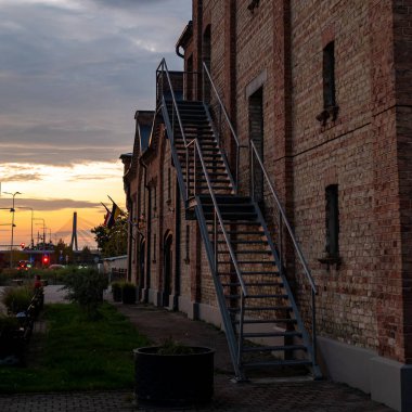 Evening scene of an old red brick building, featuring a staircase on one side that creates a strong diagonal line, visually dividing the structure and adding depth to the composition. 