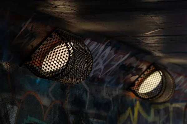 Close-up of a pedestrian tunnel light fixture, fully covered with a decorative metal grille, highlighting the geometric pattern and texture of the metal while emphasizing the urban and functional design of the tunnel lighting.