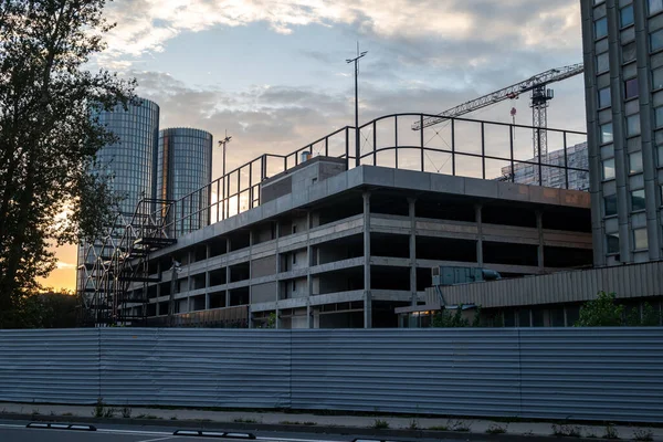 A modern building under construction in the heart of the city, surrounded by an urban environment with tower cranes working nearby. 