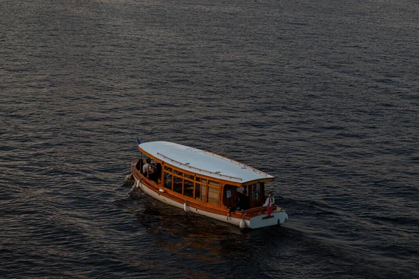 Real photograph of a wooden boat on a calm river, viewed from above, with no other objects in the frame.