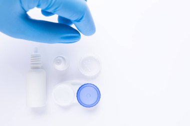 Mavi eldivenli el, beyaz arkaplandaki kontak lens tutucusunu alacak..