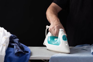 Ütü masasının üzerinde ütü yapan bir adamın eli, koyu bir arka planda..