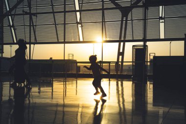 Tanınmayan bir çocuğun silueti gün doğumunda havaalanı terminalinde koşuyor..