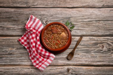 Geleneksel İspanyol mercimek güveci, yanında sucuk ve ahşap zemin üzerinde patates. Düz konum.