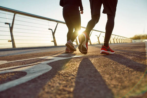 Morgonrundan. Par i sportkläder runninBak utsikt över ett par i sportkläder som löper tillsammans på bron på morgonen. Beskuren hagel tillsammans på bron på morgonen — Stockfoto