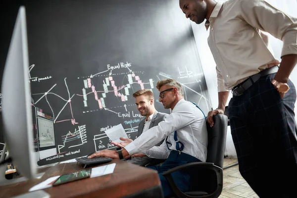 Doe open. Eerlijk waar. Hardwerkend. Drie handelaren in aandelen zijn blij met de resultaten, terwijl het kijken naar grafieken, indexen en nummers op meerdere computerschermen. Collega 's in het kantoor van de handelaren. — Stockfoto