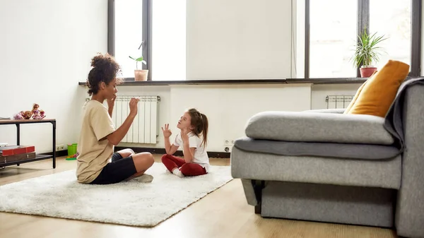 Healthcare. African american woman baby sitter and caucasian cute little girl doing yoga at home — Stock Photo, Image
