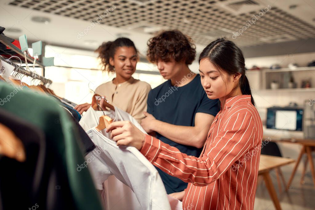 Creative people looking at already made items, while discussing logo and design of T-shirt. Young man and women at custom T-shirt, clothing printing company. Horizontal shot