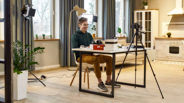 Fånga storhet. Unga glada manliga teknik bloggare ler, medan du spelar in video blogg, vlog om nya kameran lins och andra prylar sitter hemma studio. Bloggning, Arbete hemifrån koncept — Stockfoto