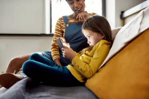 Chico listo. Mujer afroamericana niñera y niña linda caucásica usando tablet pc, sentada en casa. Educación infantil, actividades de ocio, concepto de cuidado de niños —  Fotos de Stock