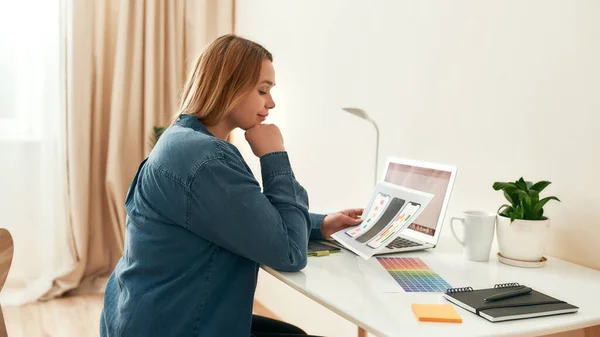 Progettazione app mobile. Vista laterale di designer donna o sviluppatore vestiti casual guardando schizzi e sorridendo mentre si lavora da casa — Foto Stock