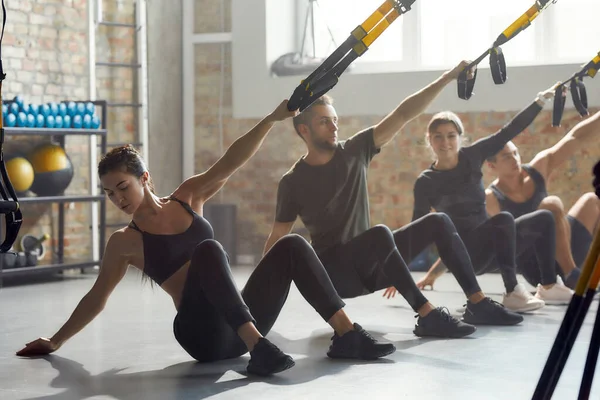 Fitness împreună. Fotografie completă a bărbaților și femeilor care fac exerciții de fitness TRX la sala de sport industrială. Push-up, concept de antrenament de grup — Fotografie, imagine de stoc