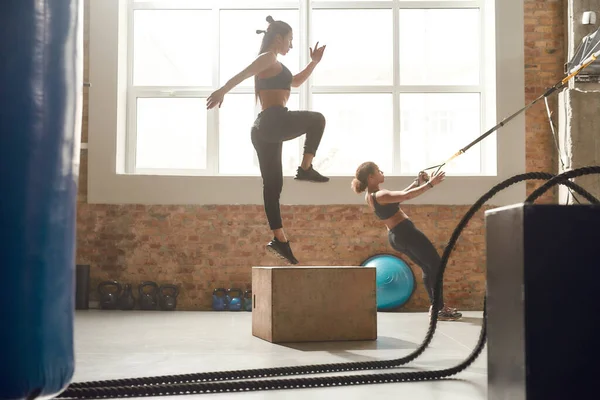 Aceite grandes desafios. Filmagem completa de mulheres esportivas fazendo exercícios no ginásio industrial. Saltando usando caixa de plyo e fazendo treinamento de fitness TRX. Formação em grupo, conceito de trabalho em equipa — Fotografia de Stock