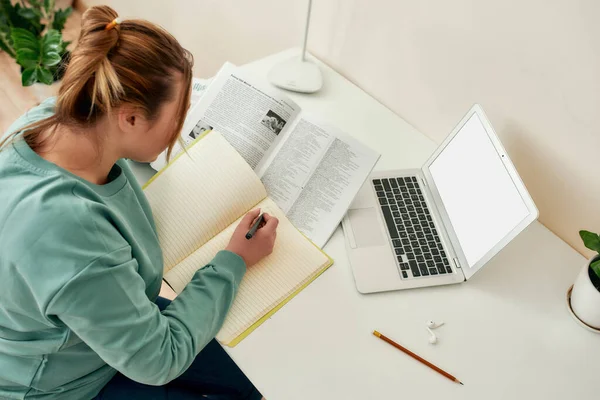 Sto facendo i compiti. Vista dall'alto della giovane studentessa seduta a tavola, che legge il manuale e prende appunti mentre studia a casa — Foto Stock