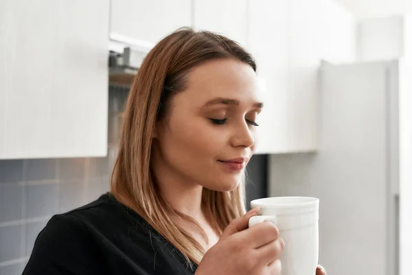 Fühlen Sie sich gut mit Kaffee. Nahaufnahme einer jungen kurvigen Frau, die ihre Augen schließt, während sie Tee oder Kaffee in der Küche trinkt — Stockfoto