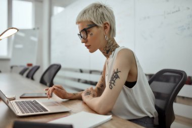 Modern iş adamı. Kısa saçlı, genç ve güzel bir kadının toplantı odasında çalışırken laptopunu kullanmasının yan görüntüsü.