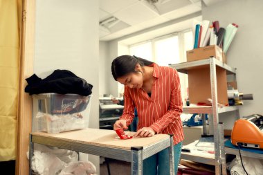 İşleme odaklan. Genç bir kadın, reklam etiketindeki desteği bir tişörte basılmaya hazırlanırken metinle kaldırıyor.
