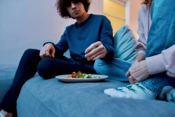 Sto mangiando dei dolci. Coppia seduta sul divano in soggiorno e mangiare colorati orsetti gommosi fruttati o marmellata, guardando la tv — Foto Stock