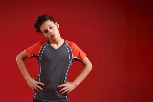 Lusta mód. Egy tinédzser fiú fitnessz szakon van, lehunyta a szemét edzés közben. Piros háttérrel elszigetelve. Sport, edzés, fitness, aktív életmód koncepció. Vízszintes lövés — Stock Fotó
