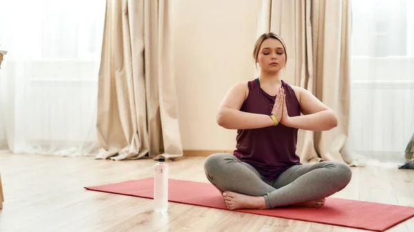 Uyumunuz için. Spor kıyafetleri içinde, evde yoga minderinde lotus pozisyonunda meditasyon yapan kıvrımlı bir kadın. — Stok fotoğraf