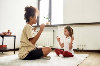 Sağlıklı bir takım kuruyorum. Afrikalı Amerikalı kadın bebek bakıcısı ve Kafkas tatlı küçük kız evde yoga yapıyorlar.