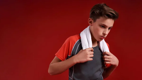 Tartsd életben az álmot. Egy tinédzser fiú sportol, félrenéz, miközben fehér törölközőt tart a kezében. Piros háttérrel elszigetelve. Fitness, tréning, aktív életmód koncepció. Vízszintes lövés. — Stock Fotó