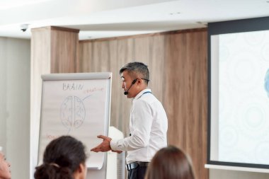 Olasılıkları geliştir. Takım elbiseli, kulaklıklı ve lazerli Asyalı erkek konuşmacı şirket toplantısında konuşma yapıyor.