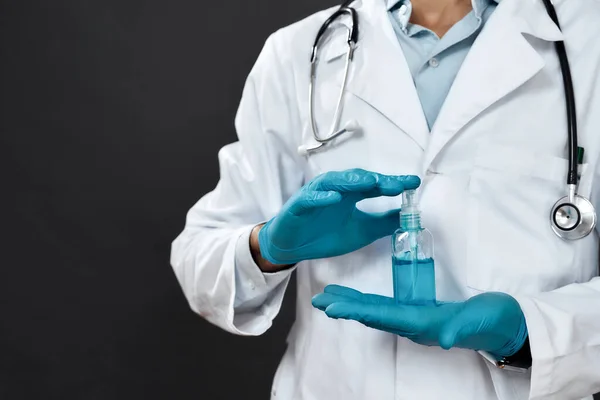 Καλλιεργημένη φωτογραφία του άνδρα γιατρού με ιατρική στολή με στηθοσκόπιο γύρω από το λαιμό κρατώντας αντισηπτικό τζελ ενώ στέκεται πάνω σε μαύρο φόντο — Φωτογραφία Αρχείου