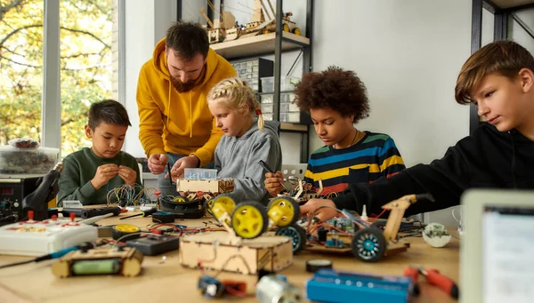 Koncentrálj a minőségre. Fiatal technikusok robotot építenek, vezetékes felszereléssel dolgoznak együtt egy férfi tanárral egy ősrobotika órán. Találmányok és kreativitás gyerekeknek — Stock Fotó