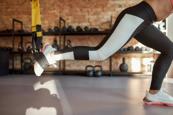 Tiro cortado de pernas de mulher esportiva esticando seu corpo usando tiras de fitness no ginásio. Esporte, conceito de estilo de vida saudável — Fotografia de Stock