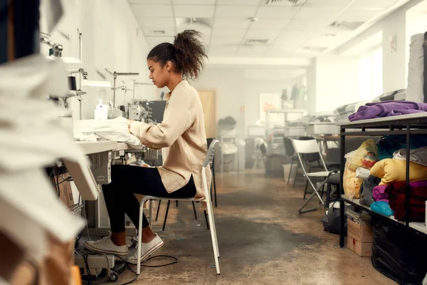 Varrni és varrni. Teljes hosszúságú felvétel fiatal varrónőkről, ahogy ülnek és varrnak. Dressmaker a varrógépen dolgozik. A szabó ruhákat készít a munkahelyén. — Stock Fotó