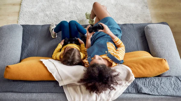 Mujer afroamericana, niñera y niña linda caucásica divirtiéndose juntos, jugando videojuegos, sentados en el sofá. Educación infantil, actividades de ocio, concepto de cuidado de niños —  Fotos de Stock