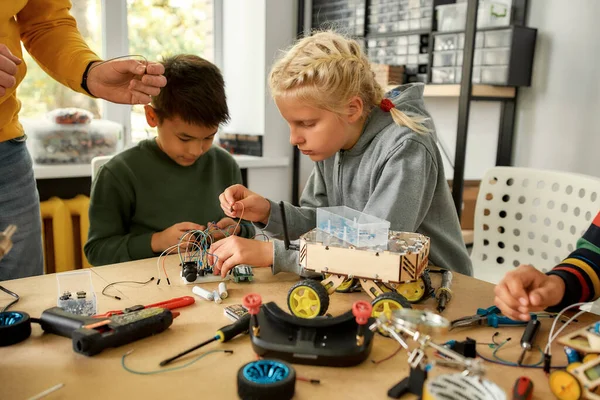 Qualität und Engineering. Junge Techniker bauen einen Roboter und arbeiten mit einem Kabelsatz zusammen mit einem männlichen Lehrer in einer Stammrobotikklasse. Erfindungen und Kreativität für Kinder — Stockfoto