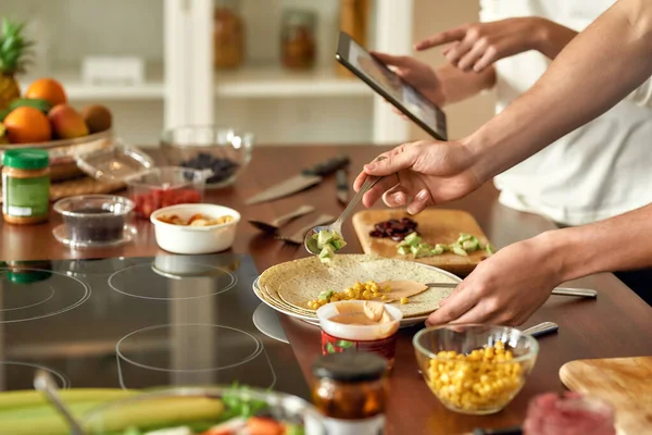 Close up of process of cooking. Man preparing meal while woman checking recipe using tablet. Vegetarians cooking in the kitchen together