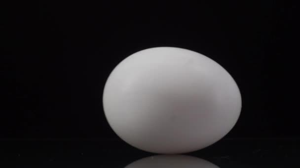 Rotation des œufs. Œuf de poulet blanc filant sur un fond noir avec réflexion. Focus principal sur l'oeuf 