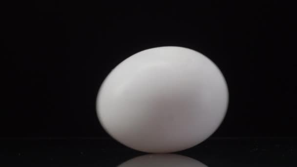 Œuf de poulet blanc filant sur un fond noir avec une belle réflexion. Fermer la vidéo 4K 
