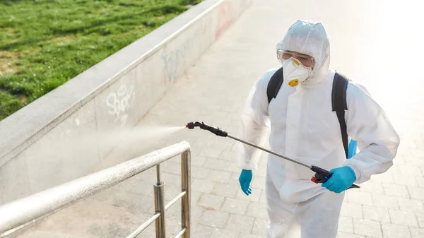 Committed to your health. Sanitization, cleaning, disinfection of the streets and alleys in the city center due to the emergence of the Covid19 virus. Man in protective suit and mask at work — Stock Photo, Image