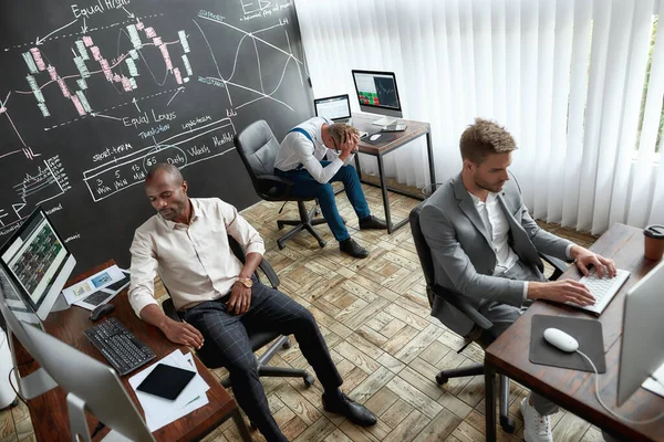 Cansancio. Vista de ángulo alto de tres comerciantes sentados junto a escritorios frente a monitores de computadora mientras trabajan en la oficina. Parecen cansados y desesperados. . — Foto de Stock