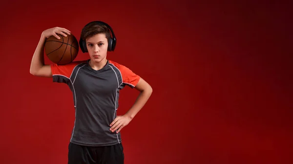 Az élet rövid, Játssz keményen. Egy sportoló tinédzser fiú a kamerába néz, miközben kosárlabdát tart a kezében. Piros háttérrel elszigetelve. Fitness, tréning, aktív életmód koncepció. Vízszintes lövés — Stock Fotó